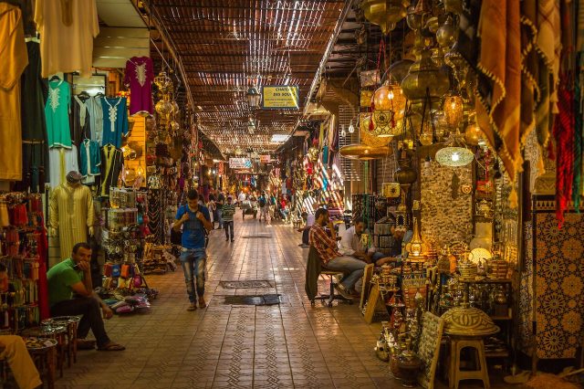 Busy Moroccan souk with vibrant stalls filled with goods, reflecting the bustling market atmosphere where tourists may encounter street vendors and potential scams.